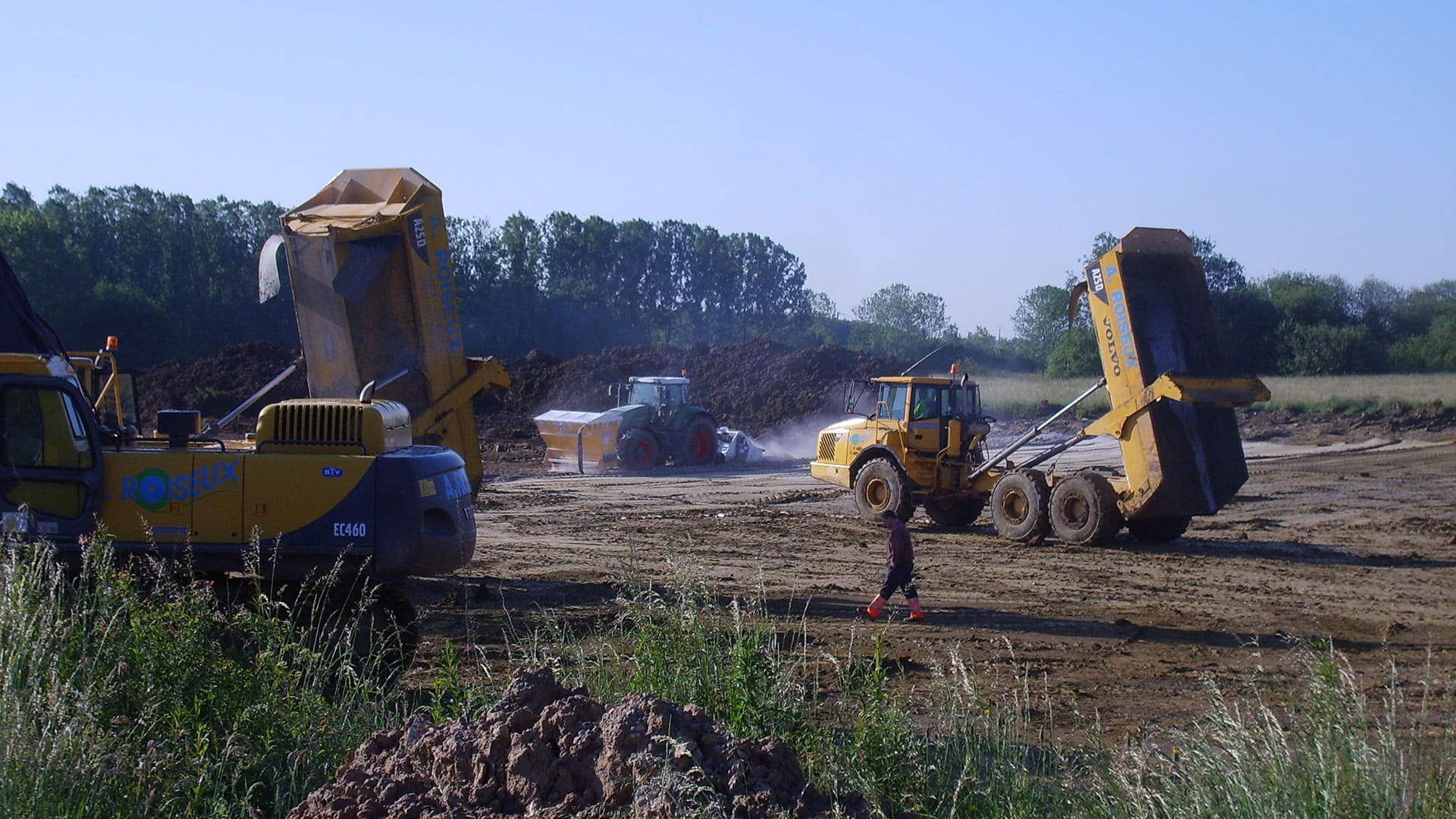 Chantier dans un champ avec plusieurs engins jaunes comme des grues et des camions benne